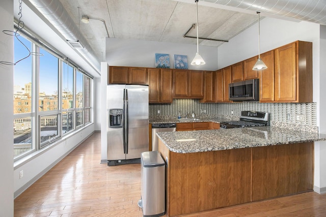 kitchen featuring a peninsula, appliances with stainless steel finishes, light wood finished floors, brown cabinetry, and decorative light fixtures