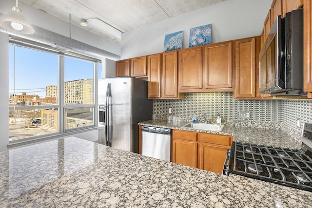 kitchen with appliances with stainless steel finishes, light stone counters, a sink, a city view, and backsplash