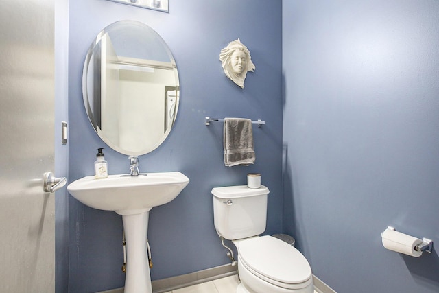 half bath featuring a sink, tile patterned flooring, toilet, and baseboards