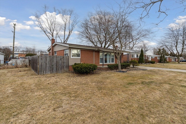 view of front of property featuring brick siding, a chimney, a front lawn, and fence