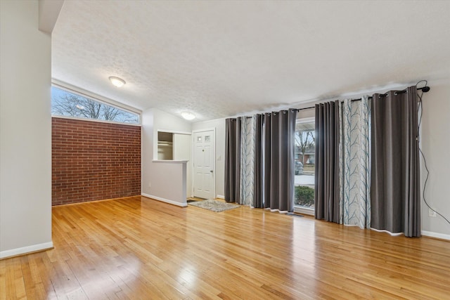 spare room with brick wall, baseboards, vaulted ceiling, a textured ceiling, and wood-type flooring