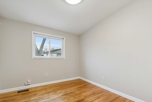 spare room with light wood-type flooring, visible vents, and baseboards