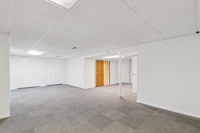 finished basement featuring a paneled ceiling, carpet floors, and baseboards