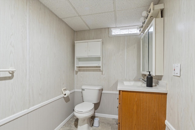 half bathroom featuring vanity, toilet, a paneled ceiling, and baseboards