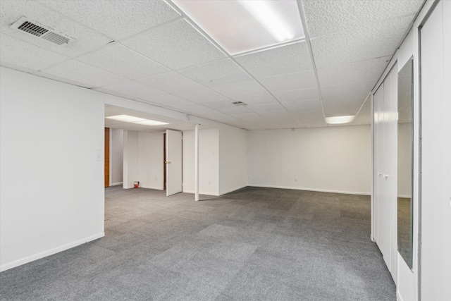 finished below grade area with visible vents, a paneled ceiling, baseboards, and carpet floors