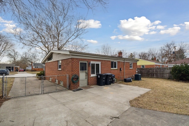 rear view of house with a gate, central AC unit, fence, a yard, and brick siding