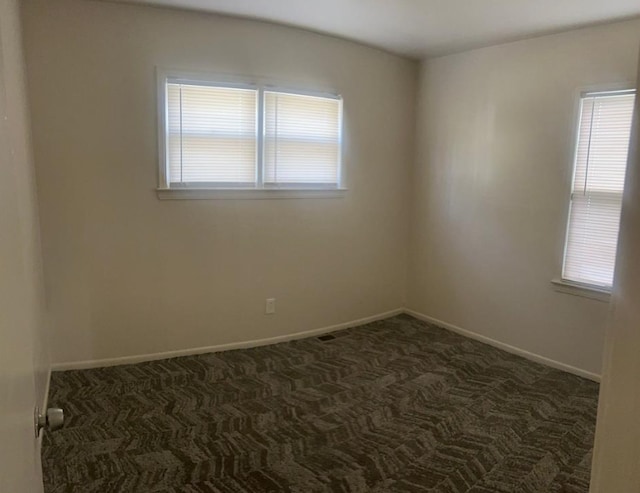 empty room featuring dark colored carpet and baseboards