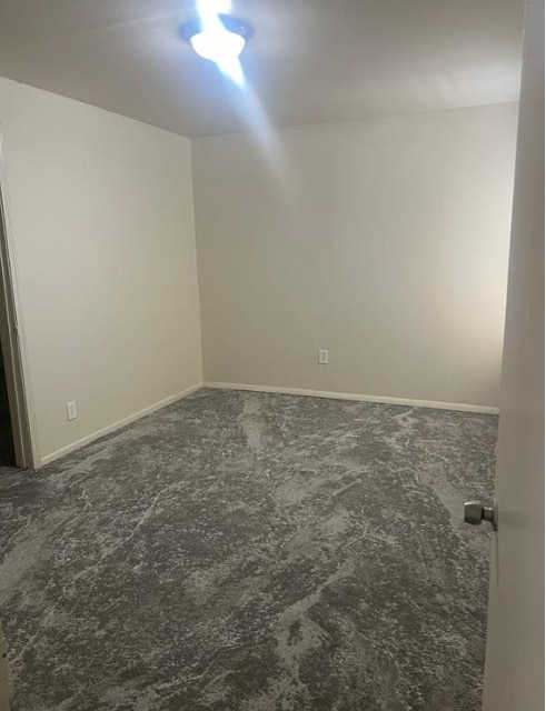 unfurnished room with baseboards and dark colored carpet