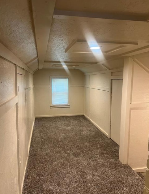 interior space with vaulted ceiling, dark colored carpet, and a textured ceiling