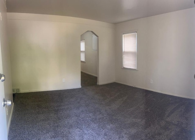 spare room featuring dark carpet, baseboards, visible vents, and arched walkways