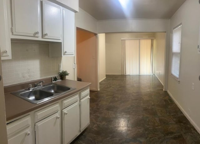 kitchen with baseboards, decorative backsplash, a sink, and white cabinets