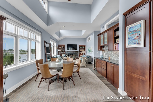 dining space featuring a fireplace, light wood finished floors, visible vents, a towering ceiling, and baseboards