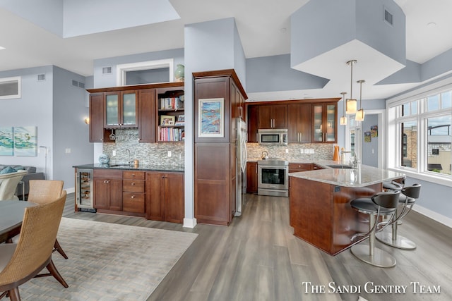 kitchen featuring light stone counters, stainless steel appliances, visible vents, hanging light fixtures, and glass insert cabinets