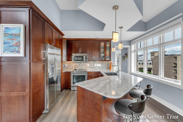 kitchen featuring glass insert cabinets, light stone counters, appliances with stainless steel finishes, pendant lighting, and a sink