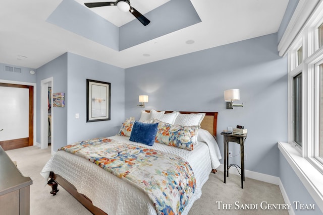 bedroom with light carpet, baseboards, visible vents, a ceiling fan, and a tray ceiling