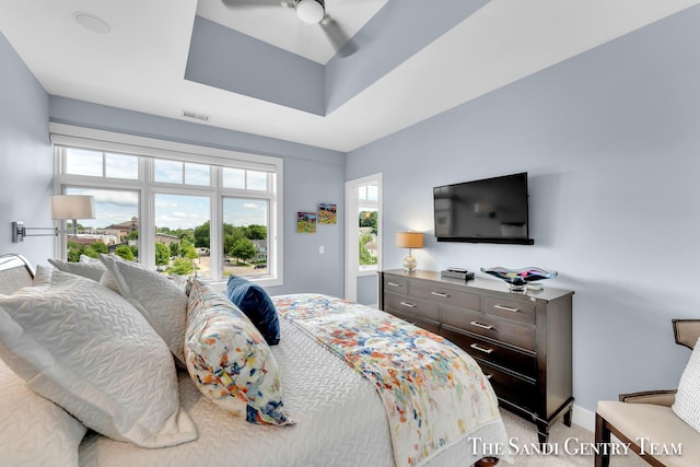 bedroom with light carpet, ceiling fan, a tray ceiling, and visible vents