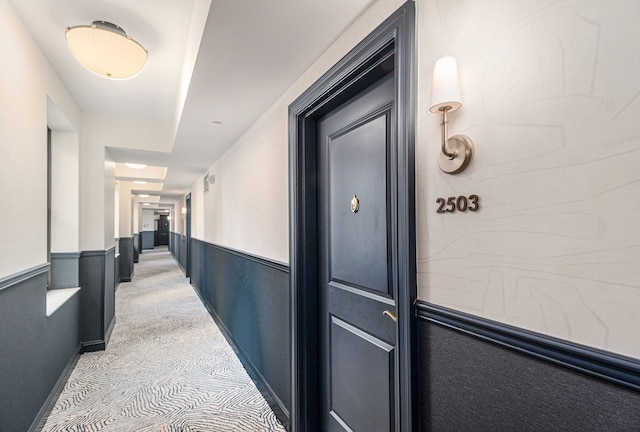 hall featuring a wainscoted wall and light carpet