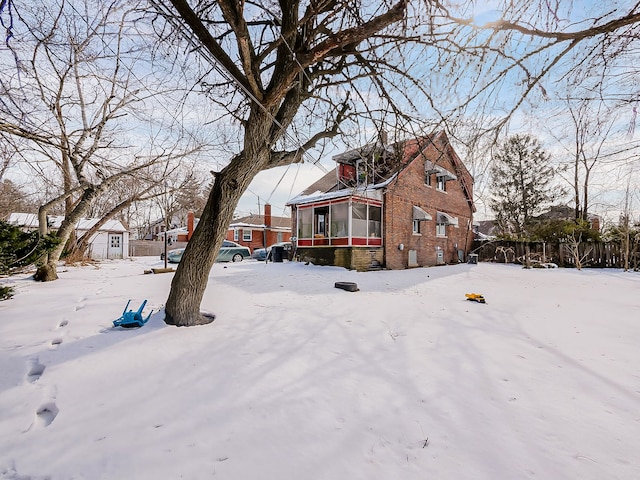 yard covered in snow with an outbuilding, a sunroom, and a storage unit