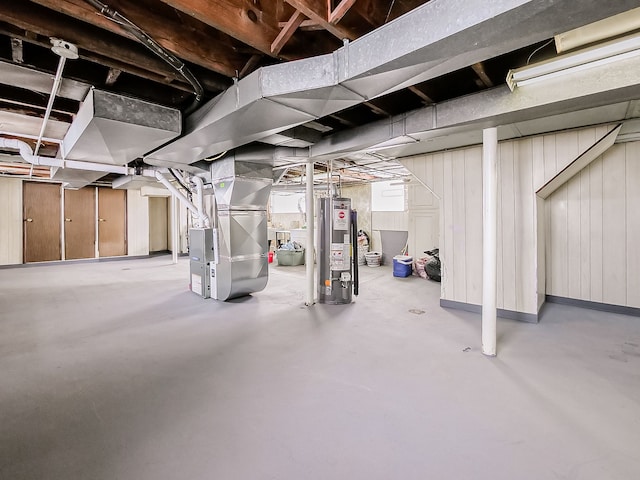 unfinished basement featuring water heater, wooden walls, and heating unit