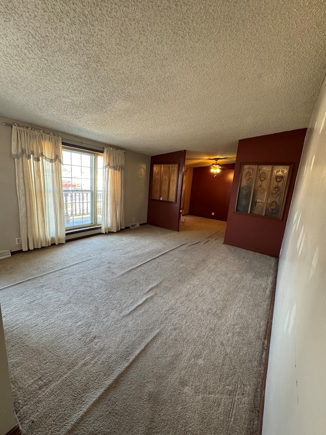 carpeted spare room featuring visible vents, ceiling fan, and a textured ceiling