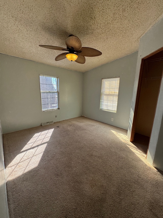 unfurnished bedroom with a textured ceiling, ceiling fan, light colored carpet, visible vents, and a closet