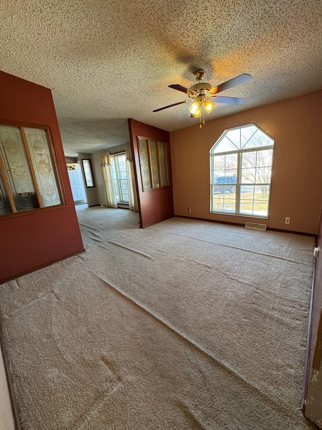 empty room featuring light carpet, ceiling fan, visible vents, and a textured ceiling