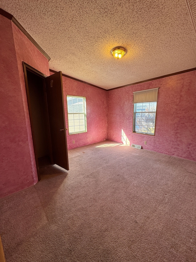 spare room with ornamental molding, carpet flooring, visible vents, and a textured ceiling