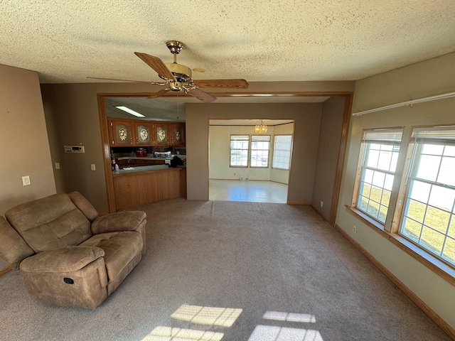 unfurnished living room featuring carpet floors, a textured ceiling, baseboards, and a ceiling fan