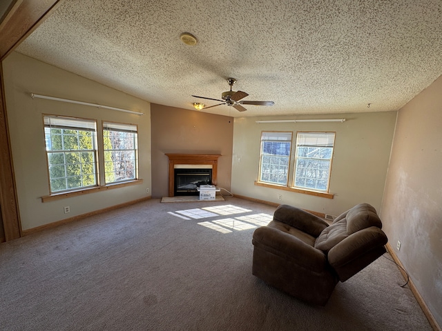 living area with a textured ceiling, a glass covered fireplace, light colored carpet, and a healthy amount of sunlight