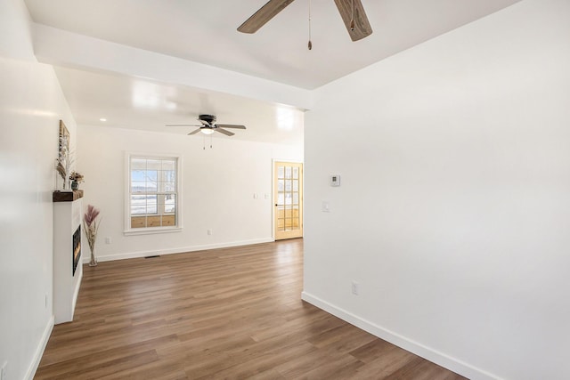 unfurnished living room with ceiling fan, a lit fireplace, wood finished floors, and baseboards