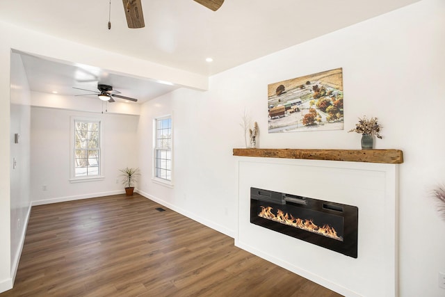 unfurnished living room featuring visible vents, baseboards, dark wood finished floors, and a glass covered fireplace