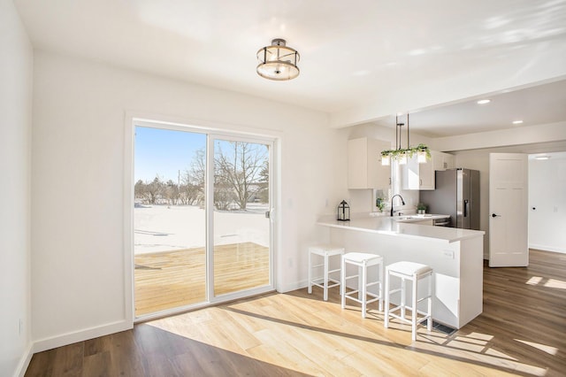 kitchen featuring white cabinets, a peninsula, hanging light fixtures, light countertops, and light wood-type flooring