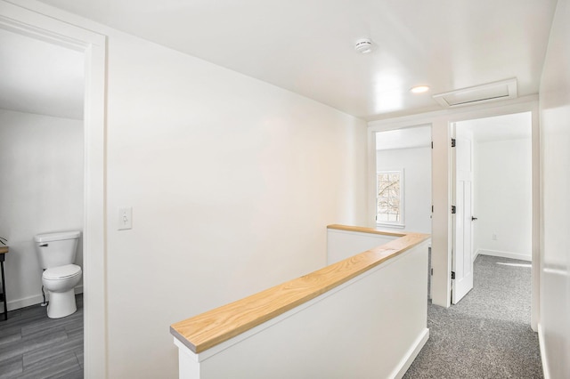 corridor featuring attic access, dark colored carpet, baseboards, and an upstairs landing