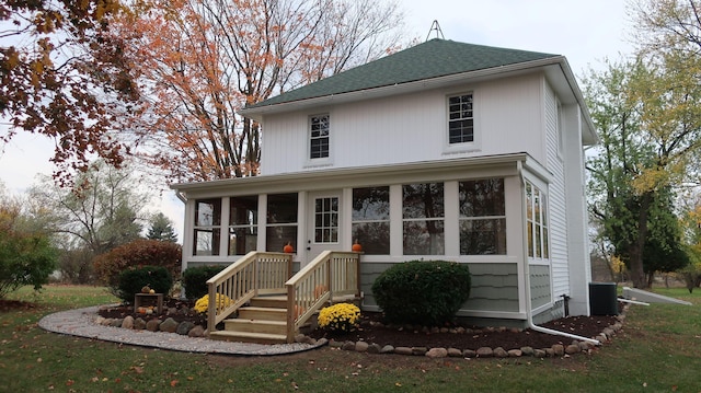 view of front of home with central air condition unit, a sunroom, roof with shingles, and a front yard