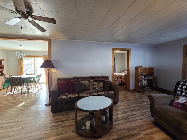 living room with ceiling fan with notable chandelier, wood finished floors, and baseboards