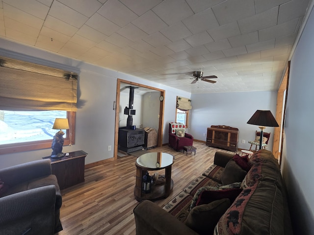 living area with a wood stove, a healthy amount of sunlight, a ceiling fan, and wood finished floors