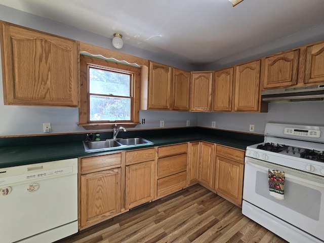 kitchen featuring white appliances, dark countertops, dark wood-style flooring, under cabinet range hood, and a sink