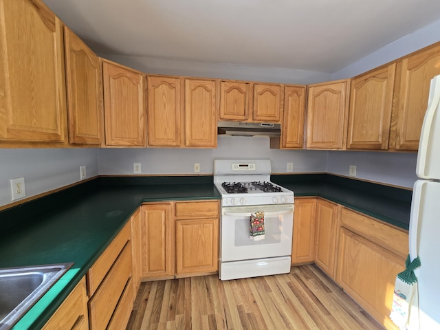 kitchen featuring white appliances, dark countertops, light wood-style flooring, under cabinet range hood, and a sink