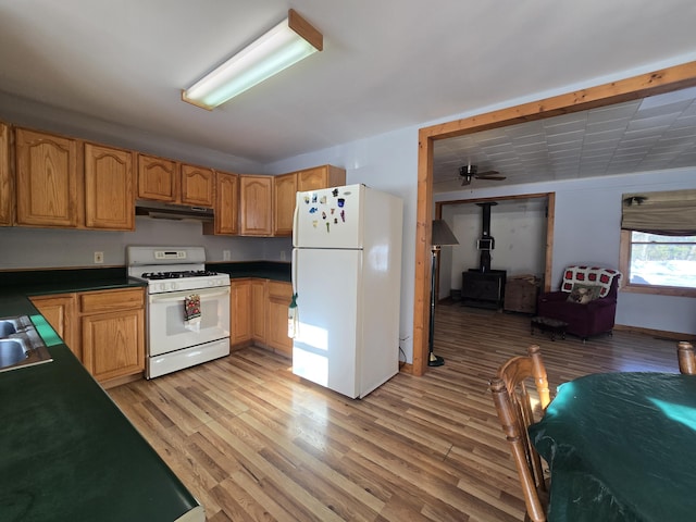 kitchen featuring under cabinet range hood, white appliances, light wood-type flooring, dark countertops, and a wood stove