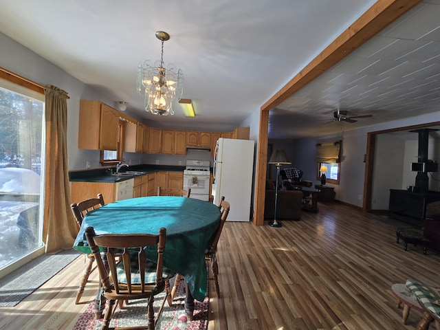 kitchen featuring pendant lighting, dark countertops, a wood stove, wood finished floors, and white appliances