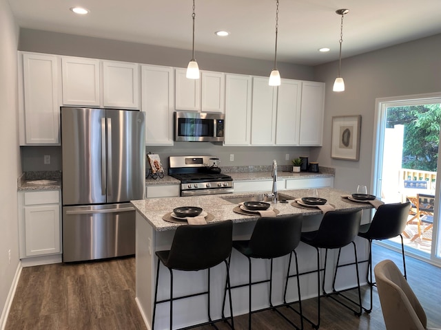 kitchen with light stone counters, dark wood-style flooring, stainless steel appliances, a kitchen island with sink, and white cabinetry