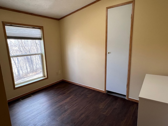 spare room featuring dark wood-style floors, crown molding, visible vents, and baseboards