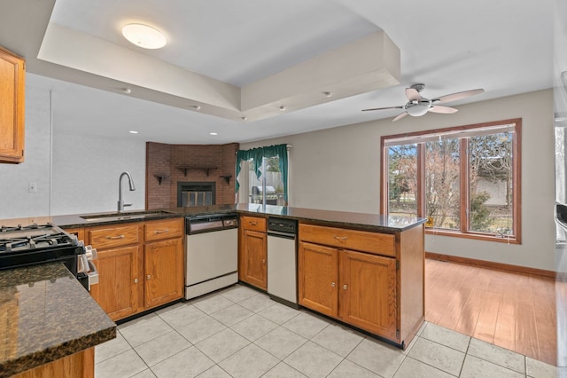 kitchen with light tile patterned flooring, a sink, dishwasher, brown cabinetry, and a raised ceiling