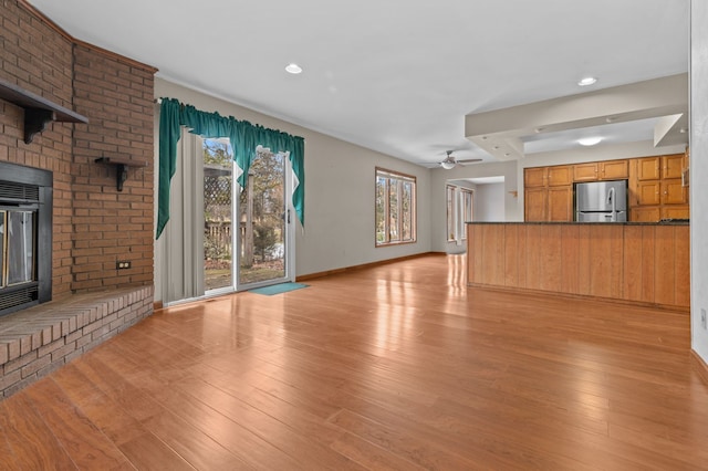 unfurnished living room with ceiling fan, light wood-type flooring, a fireplace, and baseboards