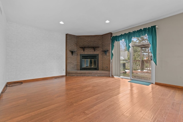 unfurnished living room featuring recessed lighting, a brick fireplace, baseboards, and wood finished floors