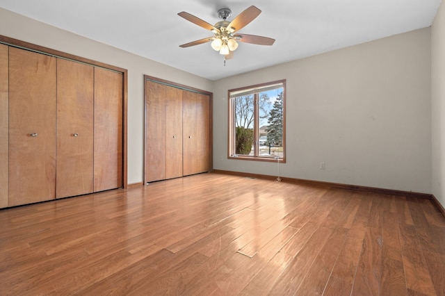 unfurnished bedroom featuring light wood-style floors, a ceiling fan, baseboards, and two closets