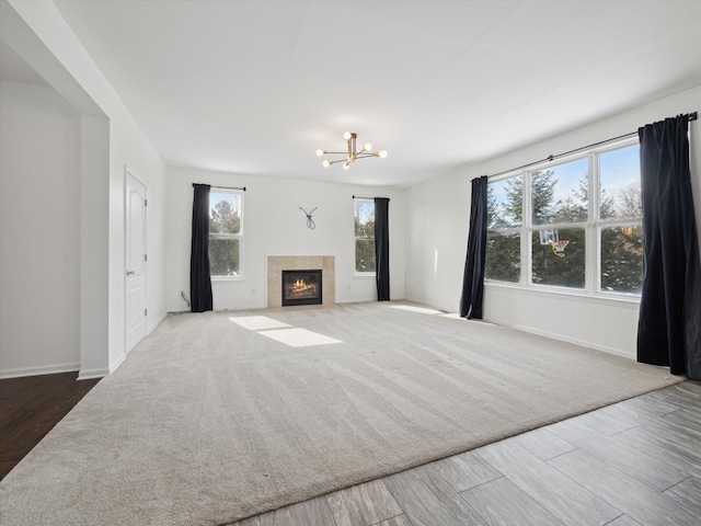 unfurnished living room featuring a chandelier, baseboards, a fireplace with flush hearth, and wood finished floors