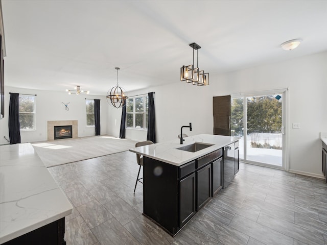 kitchen featuring dark cabinets, a sink, stainless steel dishwasher, a glass covered fireplace, and an inviting chandelier