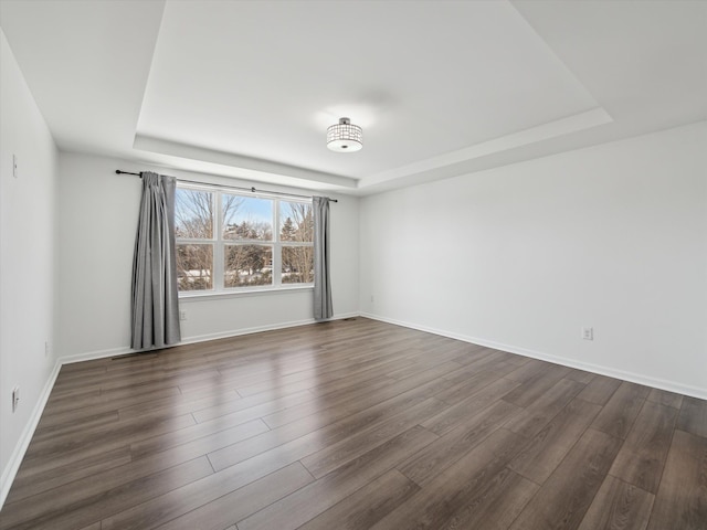 spare room featuring dark wood-style floors, a tray ceiling, and baseboards