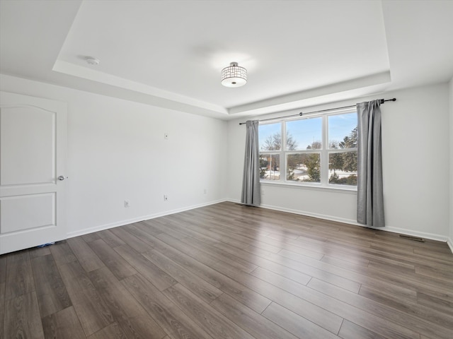 unfurnished room with baseboards, visible vents, a tray ceiling, and dark wood-style flooring